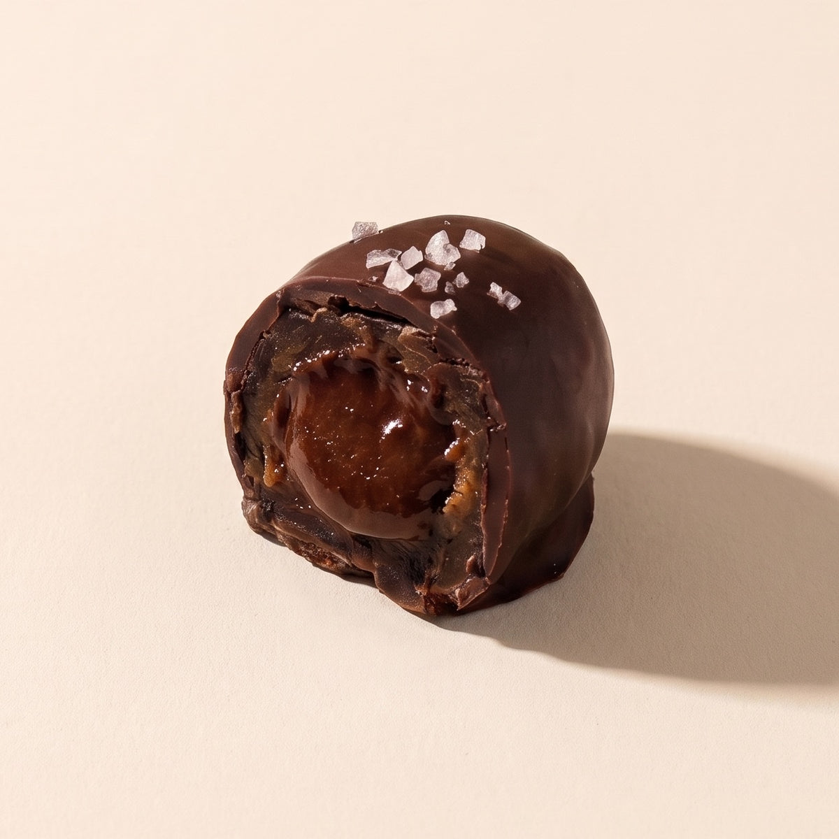 A Hot Date split open on warm plaster, showing the caramel spiced sunflower butter filling inside its dark chocolate shell, with flaked sea salt on top