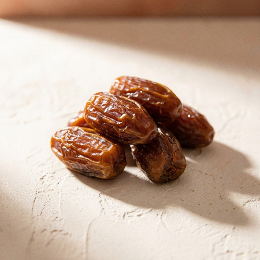 A small pile of whole California Medjool dates on a warm plaster surface, showing their wrinkled amber brown skin